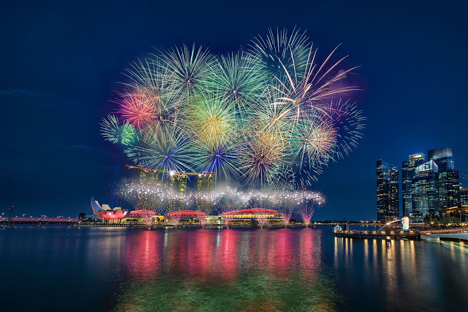 Emerald and teal fireworks cluster over the city skyline